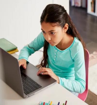 A young student with dark hair types on her laptop