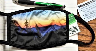 A mask next to a pen that says North Marion and a business card with the NM logo