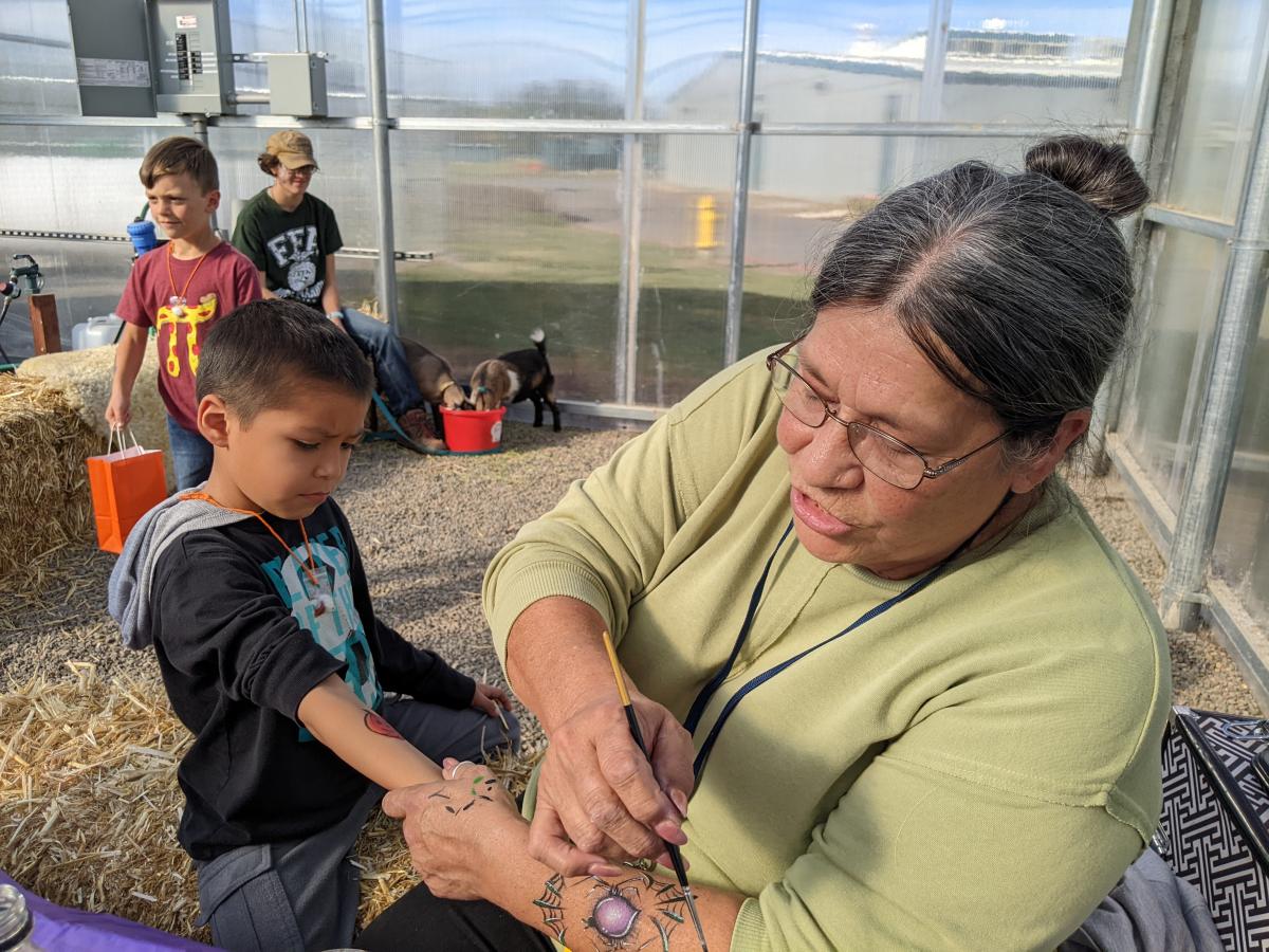 Volunteer Glenda Creekmore paints Axel Camacho Flores’s arm as Kelvin Gerdes walks past and Denali Bosco tends to the goats.