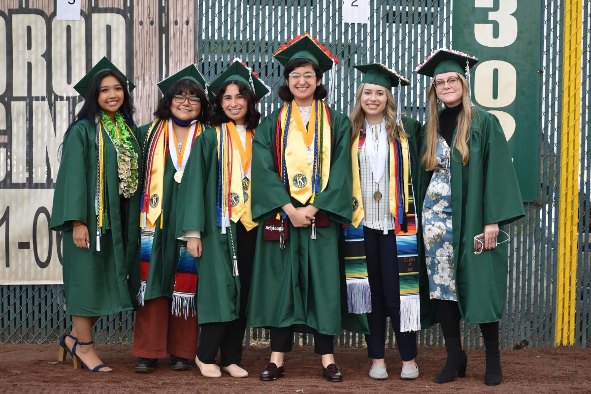 Graduates wearing caps and gowns beam for the photo