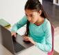 A young student with dark hair types on her laptop